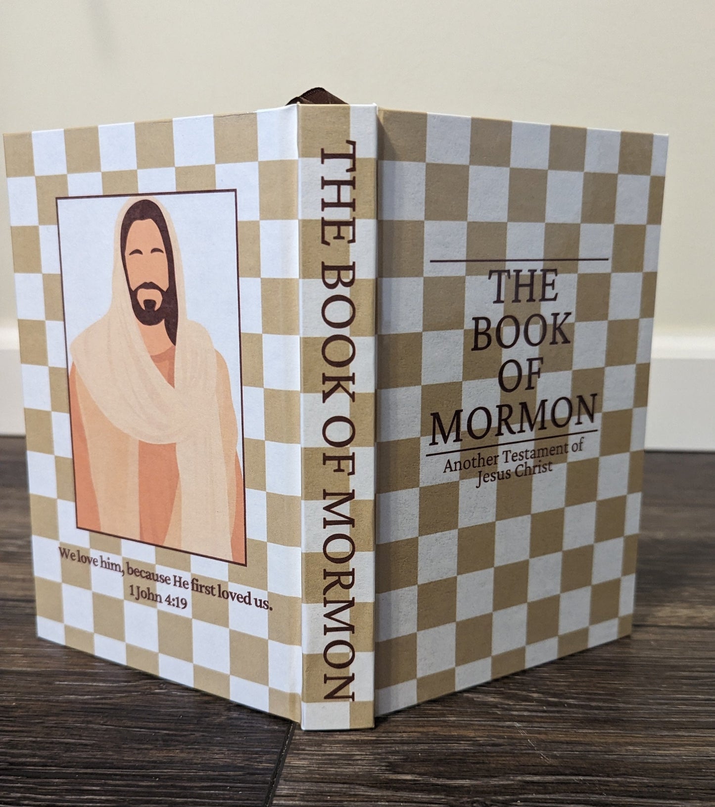 Book titled 'The Book of Mormon' with a checkered cover on a wooden surface. Checkered design is light brown and white.