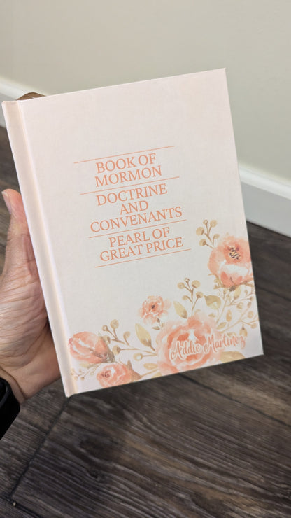 Book of Mormon with floral design held by a hand on a wooden floor.