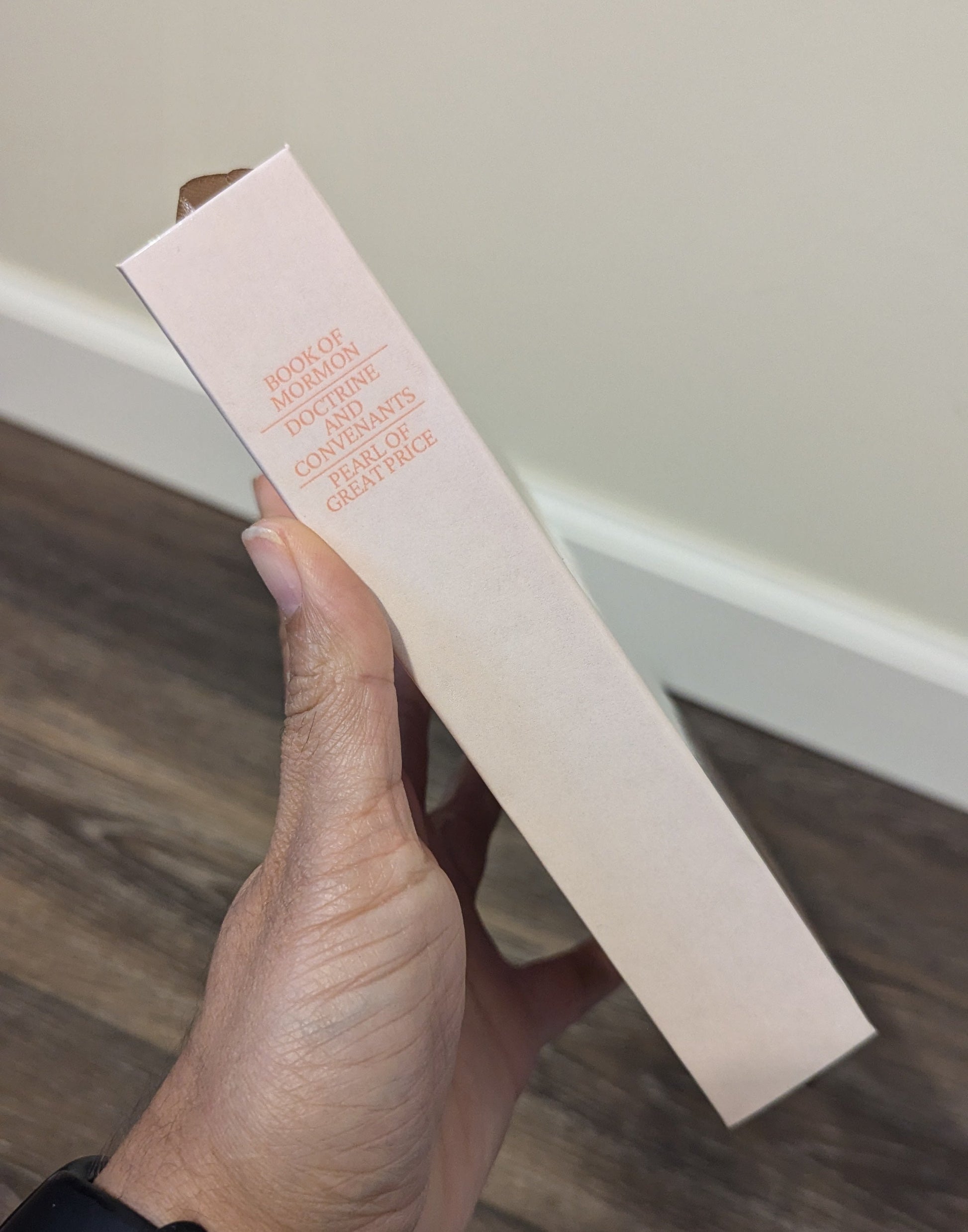 Hand holding a rectangular product box with text on a wooden floor.