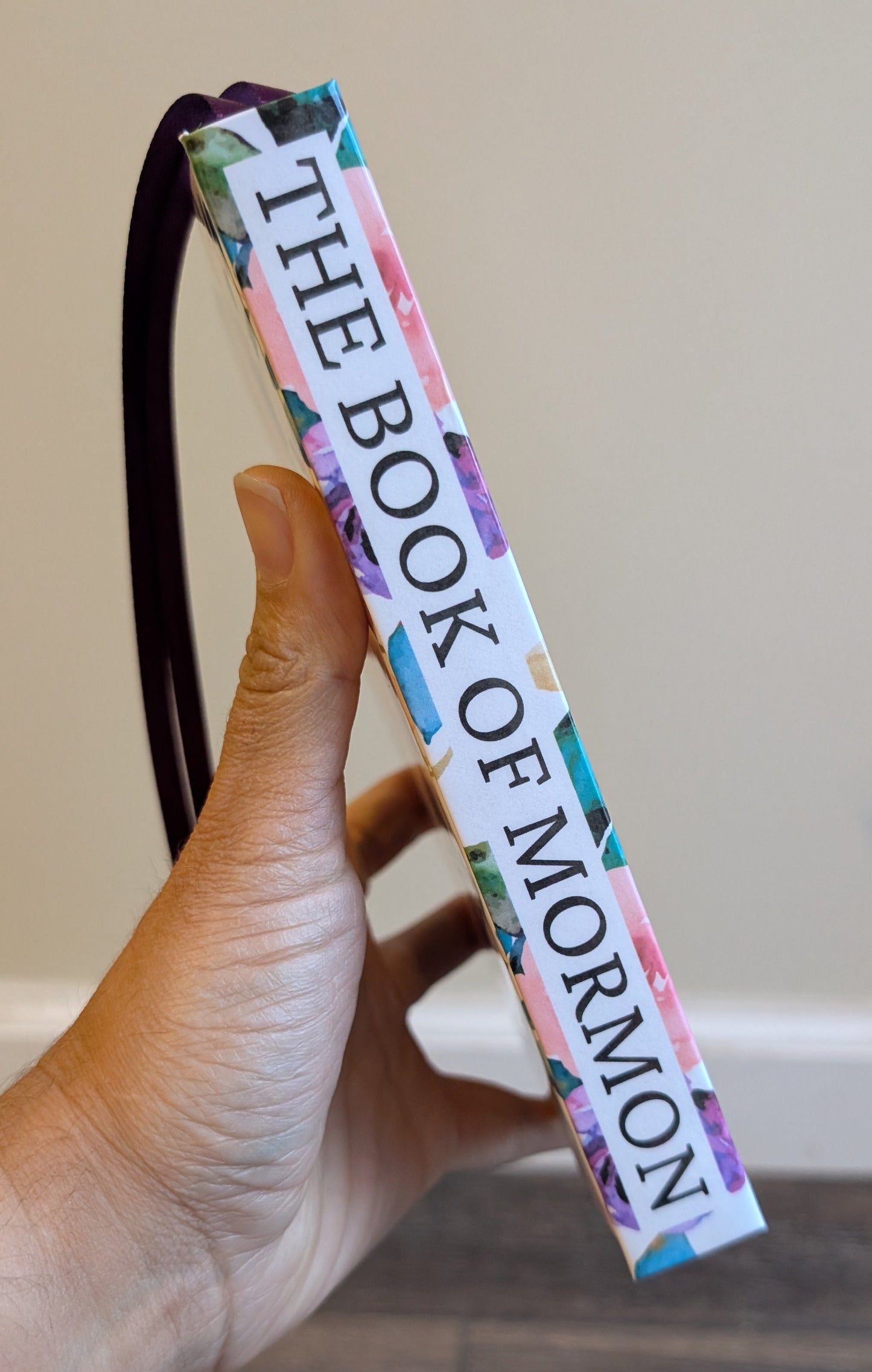 Hand holding a colorful 'The Book of Mormon' bookmark against a neutral background