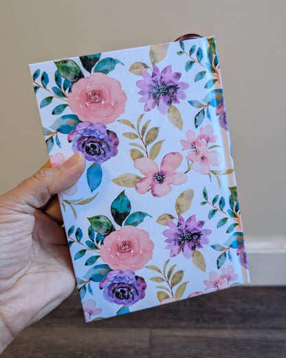 Hand holding a floral Book  of Mormon against a neutral background