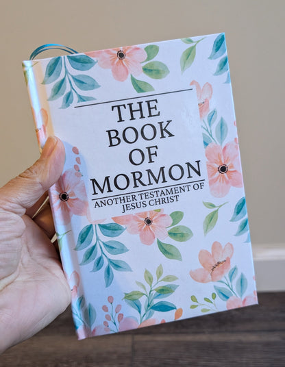 Book of Mormon with floral design held by a hand on a wooden surface