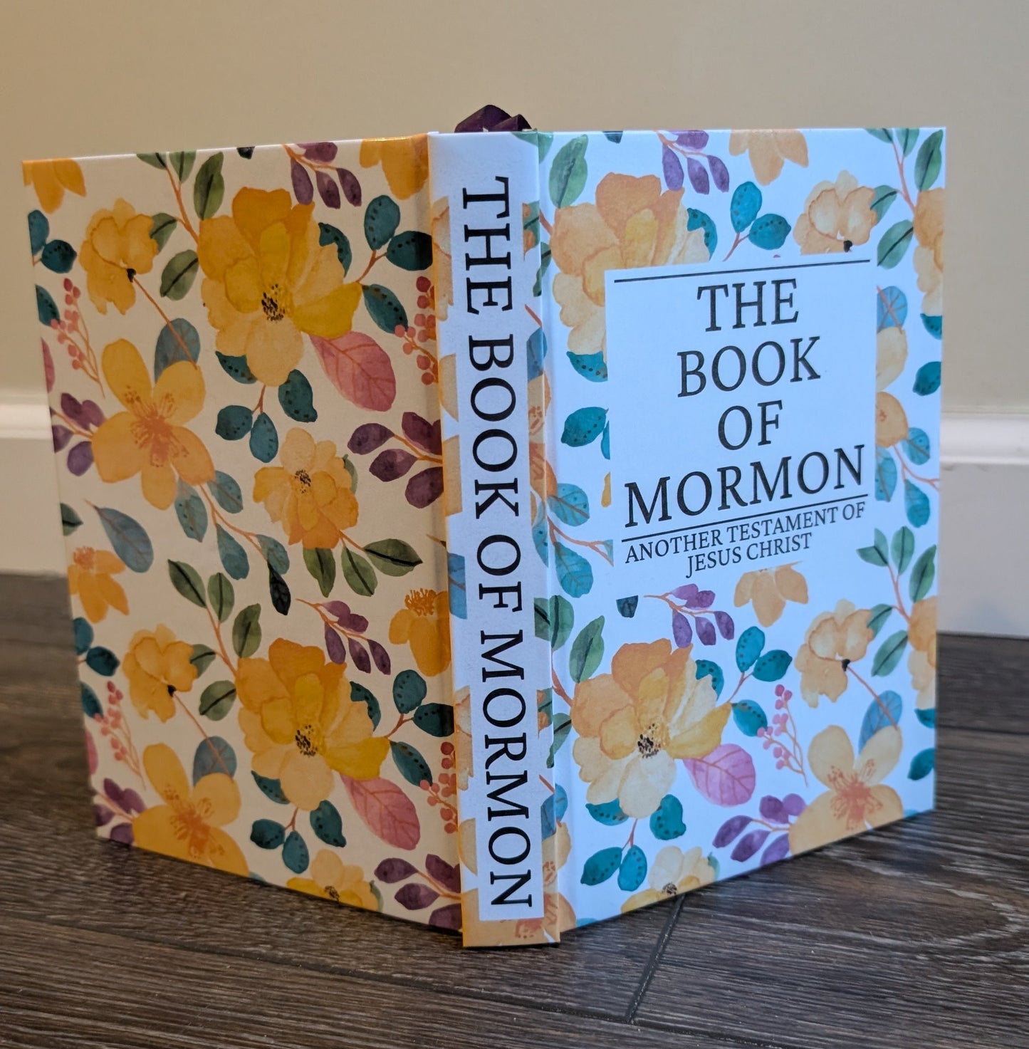 Floral-patterned book cover of 'The Book of Mormon' on a wooden surface.