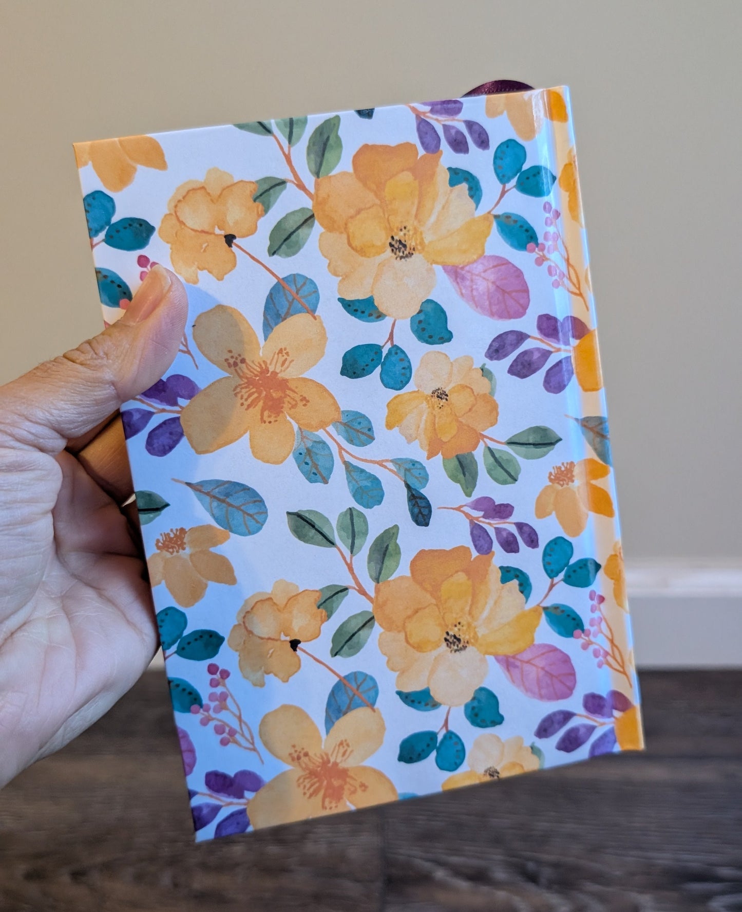 Hand holding a floral notebook with yellow flowers on a wooden surface