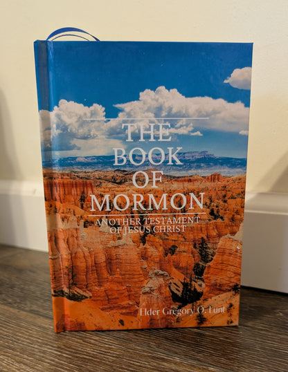 Book of Mormon on a wooden surface with a scenic cover featuring the grand canyon.