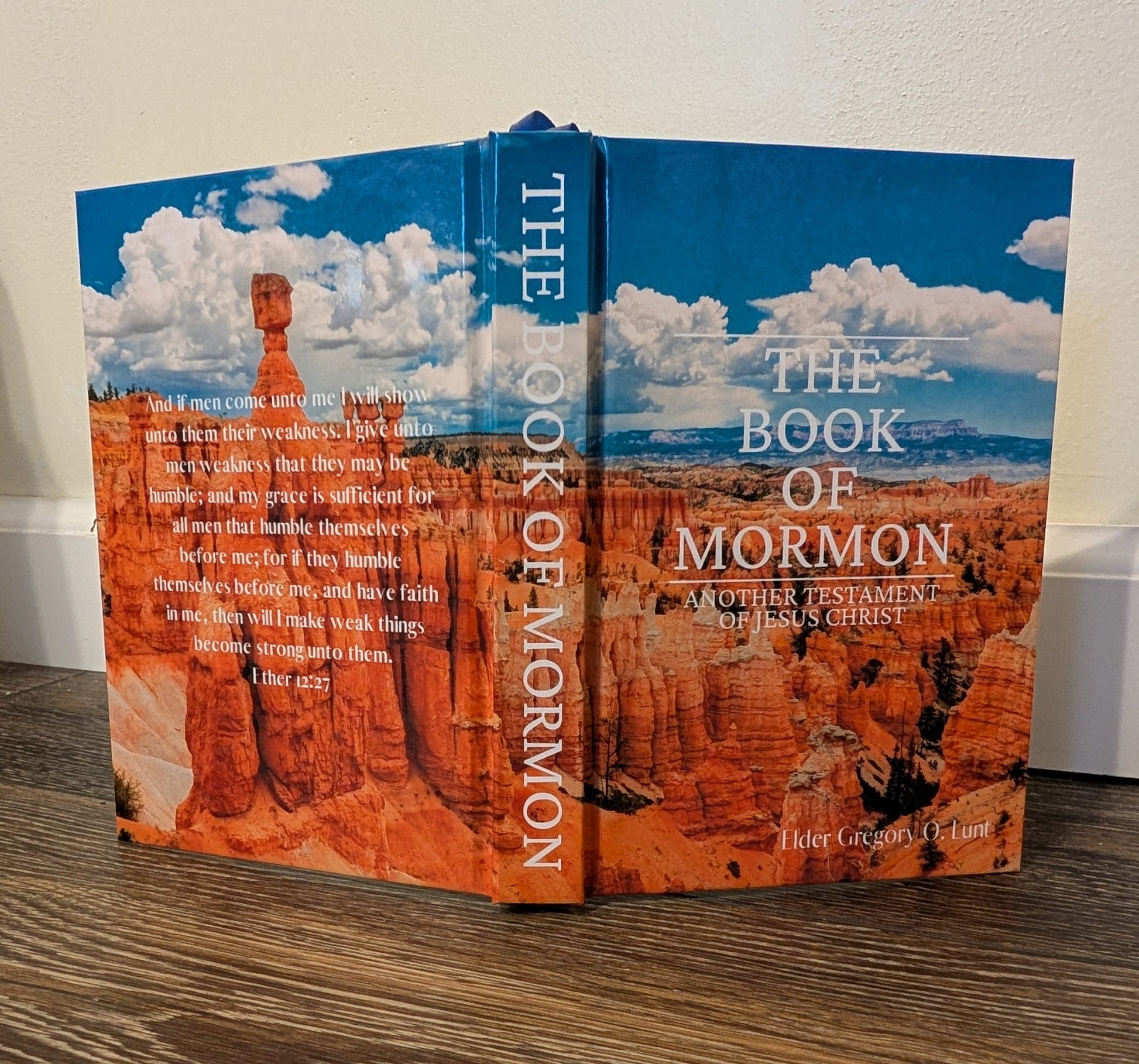 Book titled 'The Book of Mormon' on a wooden surface with a white background. The background of the Book of Mormon features the grand canyon.