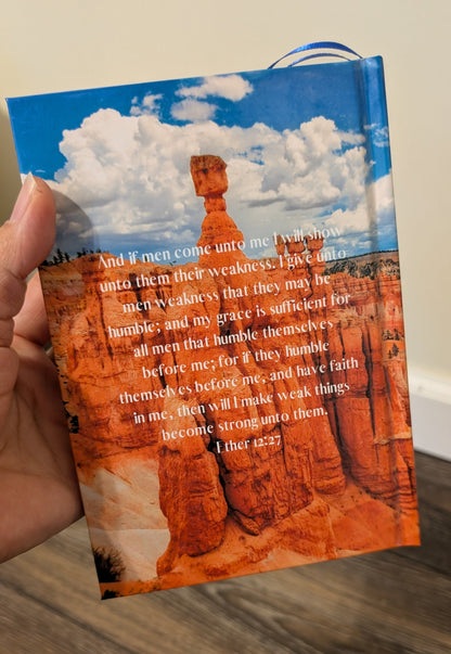 Back of Book of Mormon with a scenic cover featuring the grand canyon held by a hand on a wooden surface.