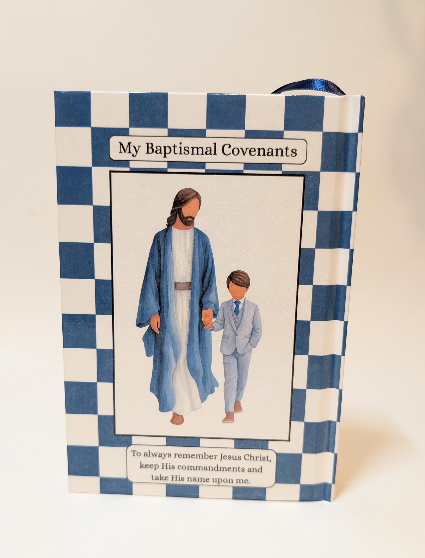 Back of a Book of Mormon titled "My Baptismal Covenants" with a blue-and-white checkered border and an illustration of Jesus and a child on the front, photographed against a plain light background.