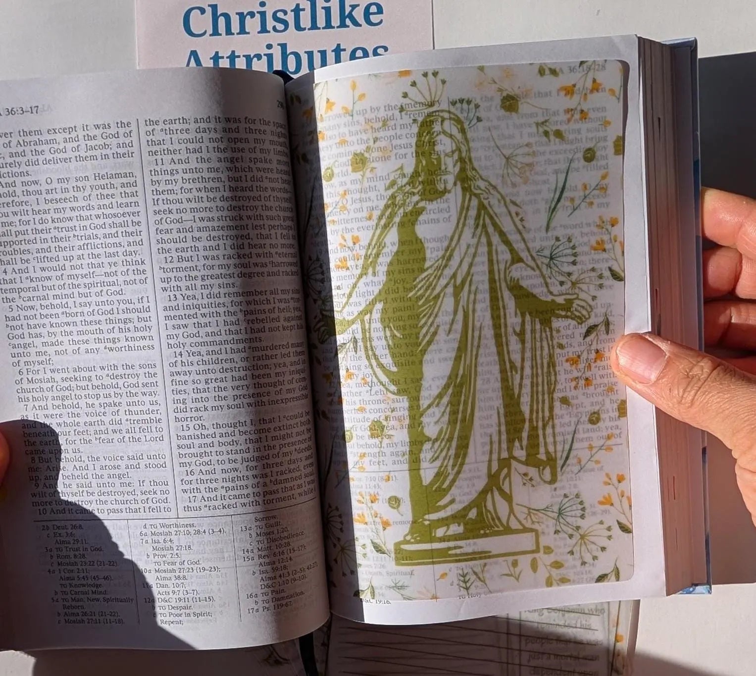 An open book with a vellum sheet inside of it. The vellum sheet depicts a picture of Christ with His hands and arms extended.